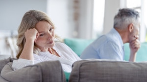 Mature couple fighting at home sitting on the sofa. They are both looking angry and frustrated.