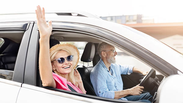 Retired couple on a road trip with the woman cheering excitedly, symbolizing the joy and freedom of being married and traveling together