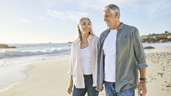 Smiling couple walking at beach on sunny day. Mature man and woman are on summer vacation. They are wearing casuals.