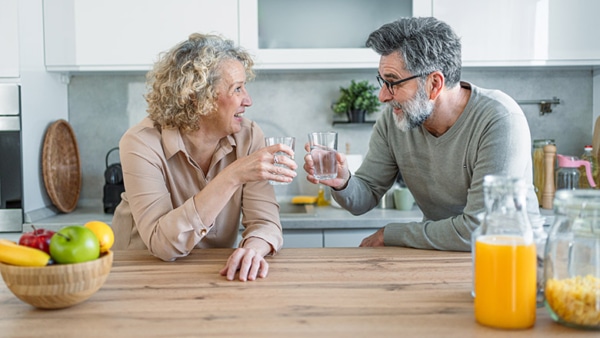Cheerful mature couple drinking water and relaxing in the kitchen at home