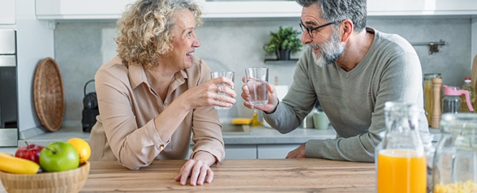 Cheerful mature couple drinking water and relaxing in the kitchen at home