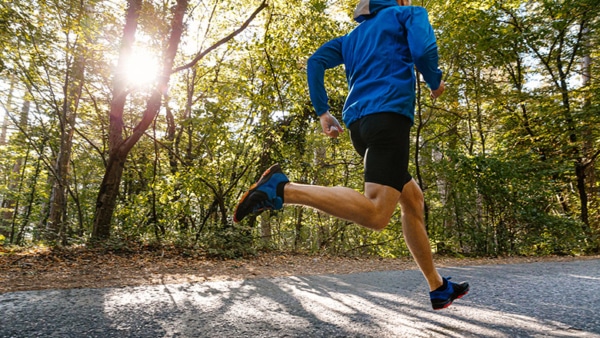 male runner running road in park in light of sun